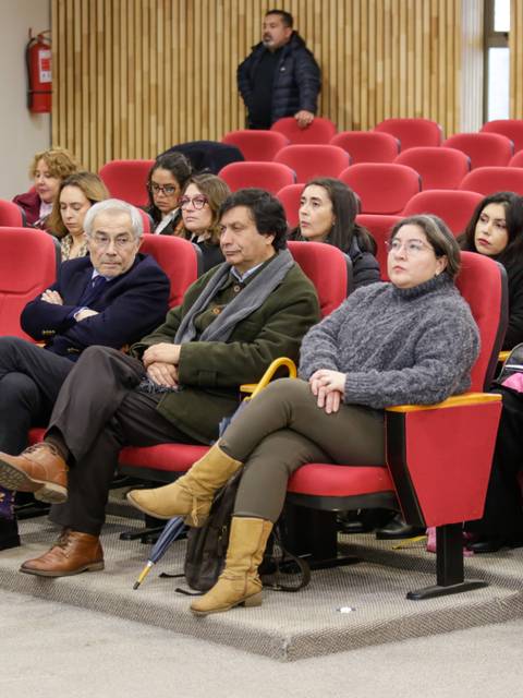 Un grupo de personas sentadas en un auditorio con sillas rojas, prestando atención a una charla o presentación.