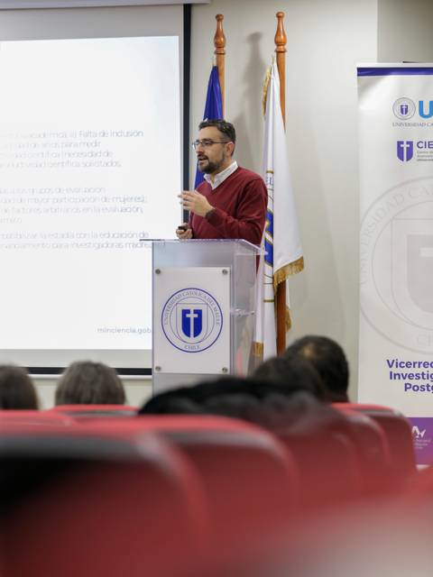 Un orador presenta información en una sala llena de asistentes.