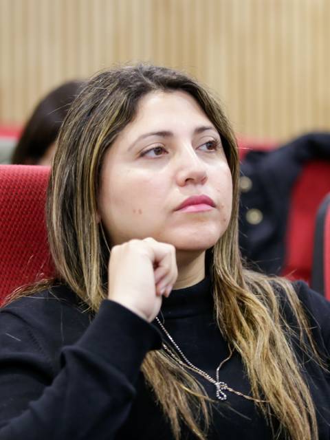 Mujer reflexionando mientras escucha en un aula.