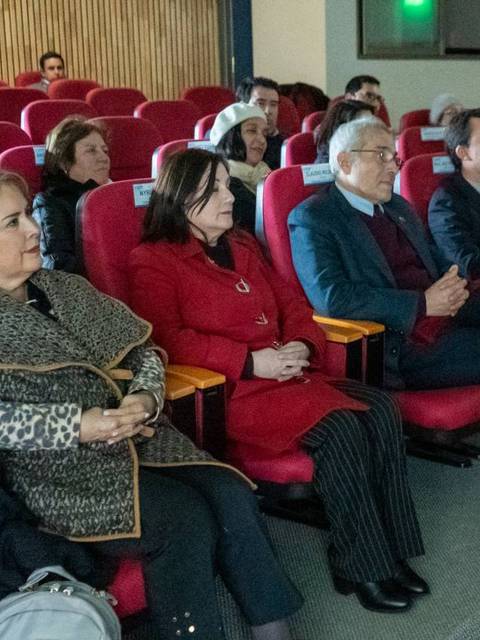 Un grupo de personas sentadas en un auditorio con butacas rojas, prestando atención en una presentación.