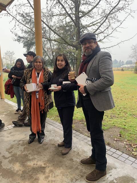 Un grupo de tres personas sonríen mientras sostienen tazas en un entorno al aire libre.