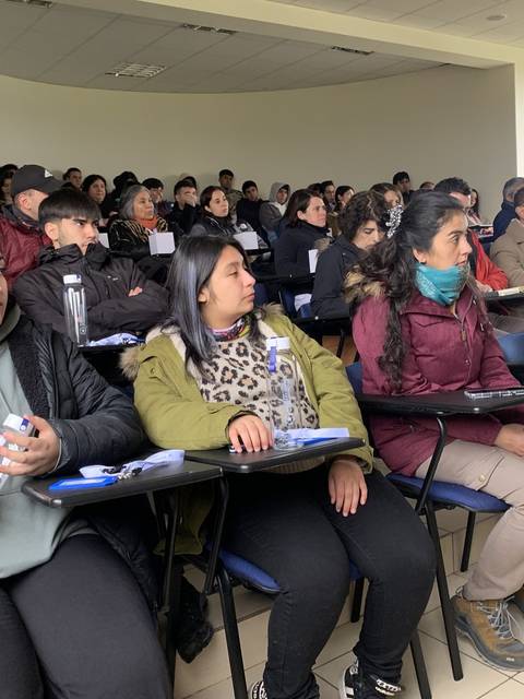 Un grupo de estudiantes y personas sentadas en un aula durante una presentación.