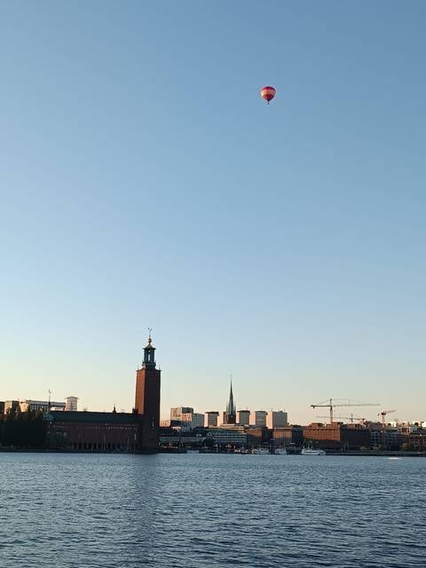 Una vista de un edificio al lado de un lago con un globo aerostático en el cielo.