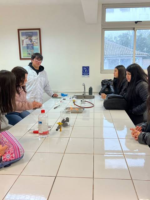 Un grupo de estudiantes observa a un profesor en un laboratorio mientras realizan una actividad científica.