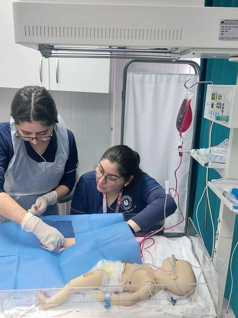 Dos estudiantes de medicina están practicando en un simulador de bebé en un entorno clínico.