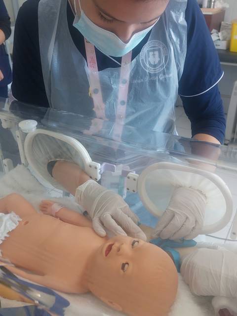 Una persona está atendiendo un muñeco de práctica en un entorno médico.