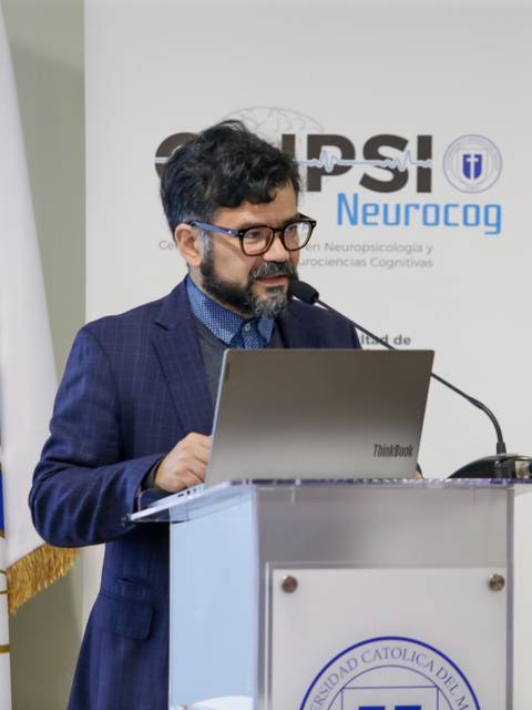 Un hombre está dando una presentación en un evento con banderas al fondo.