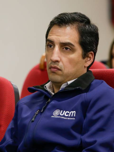 Un hombre con sudadera azul observa atentamente durante una presentación en un auditorio.