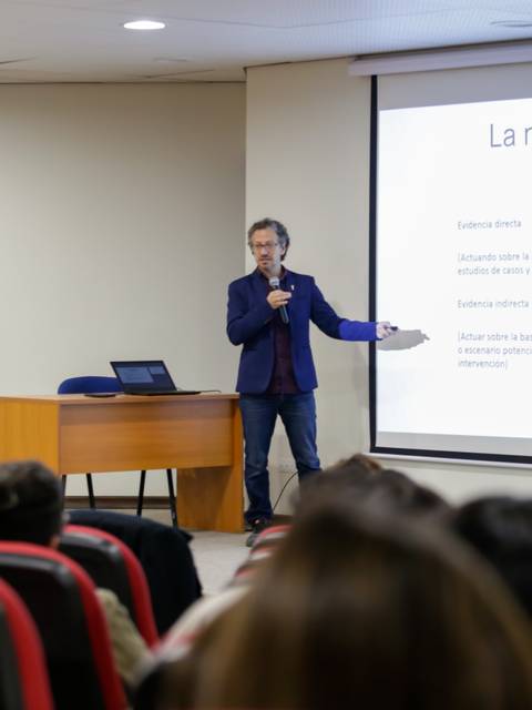 Un presentador está exponiendo un tema sobre la naturaleza de la evidencia en una conferencia con audiencia.