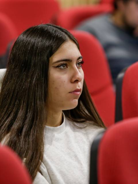 Una joven con cabello largo y lacio observa atentamente en un ambiente de aula.
