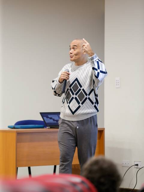 Un hombre habla con entusiasmo mientras sostiene un micrófono en un entorno de presentación.