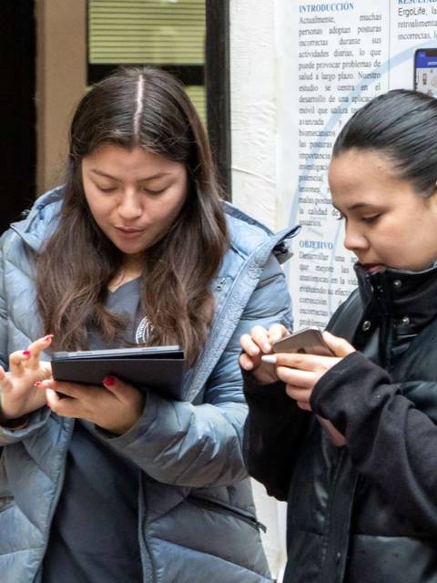 Dos mujeres observan sus dispositivos móviles en un entorno interior.