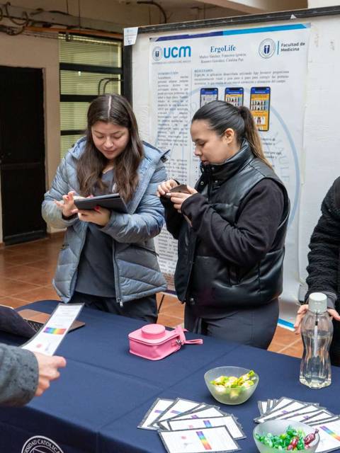 Un grupo de personas interactúa en un evento, usando dispositivos electrónicos y revisando folletos sobre técnicas de comunicación.