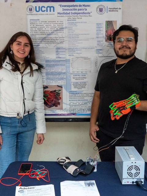 Dos personas posan frente a un cartel de investigación sobre un dispositivo para mejorar la movilidad independiente.