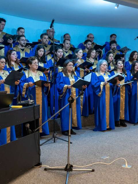 Un coro de personas vestidas con túnicas azules canta en un escenario.