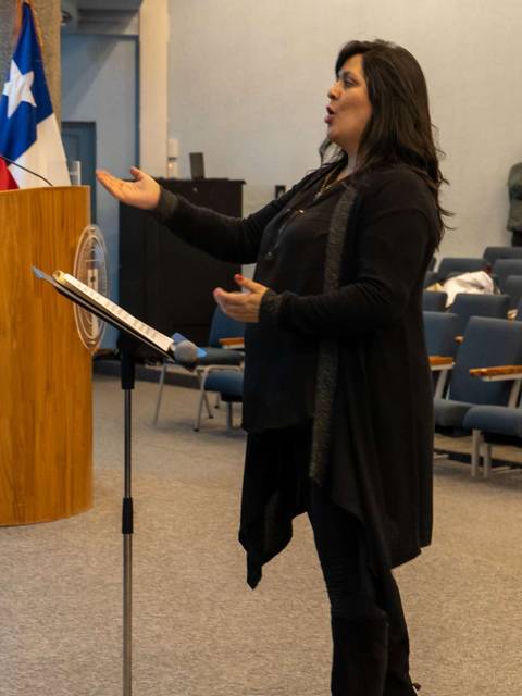 Mujer de pie hablando en un auditorio con una bandera chilena al fondo.