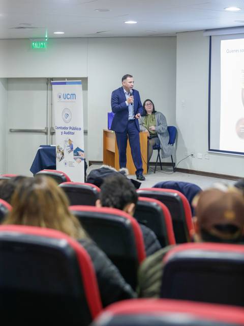 Un ponente está presentando en un evento mientras una audiencia lo escucha atentamente.