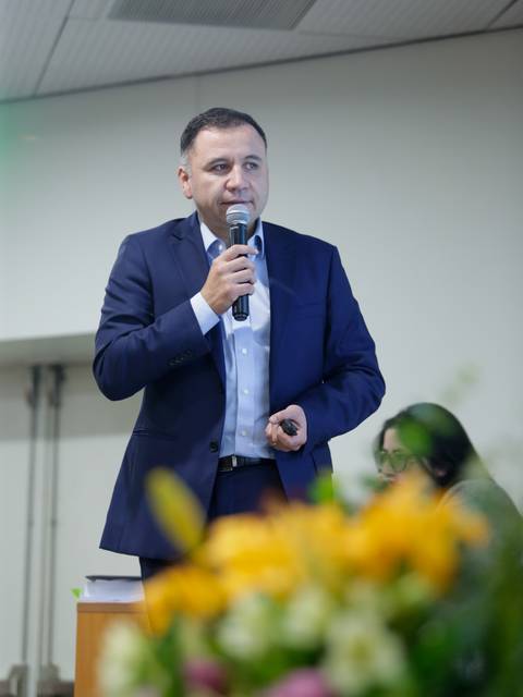 Un hombre está hablando en un evento mientras sostiene un micrófono.