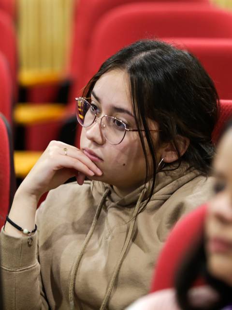 Una joven pensativa escucha atentamente en un auditorio.