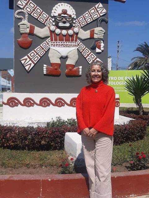 Una mujer con suéter rojo posa frente a un gran monumento decorativo en un parque.