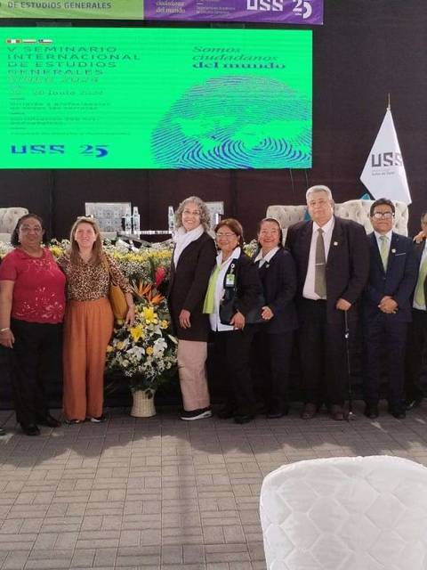 Un grupo de personas posando en un evento formal con banderas y decoraciones de fondo.