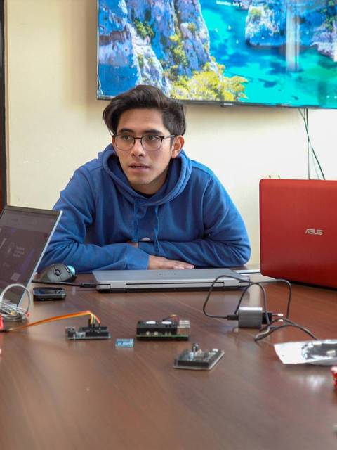 Un grupo de personas se encuentra reunido en una mesa de trabajo con computadoras y dispositivos electrónicos.