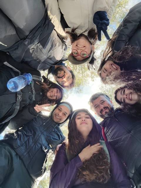 Un grupo de amigos sonríe en un círculo mientras se toman una foto al aire libre.