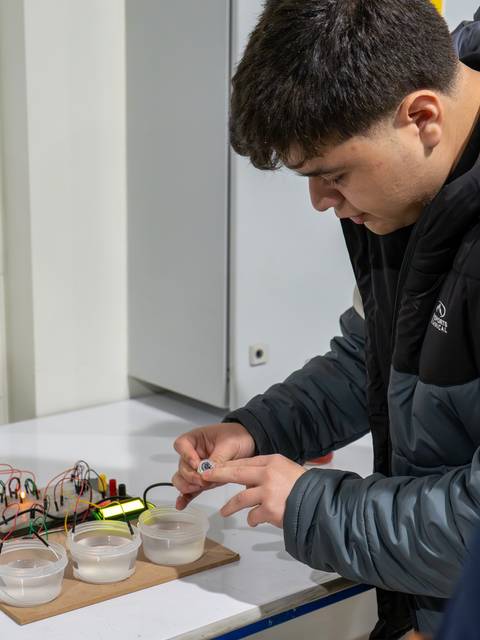Un estudiante está realizando un experimento con agua y componentes electrónicos en un laboratorio.