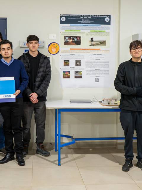 Un grupo de estudiantes posando frente a un póster en una presentación escolar.