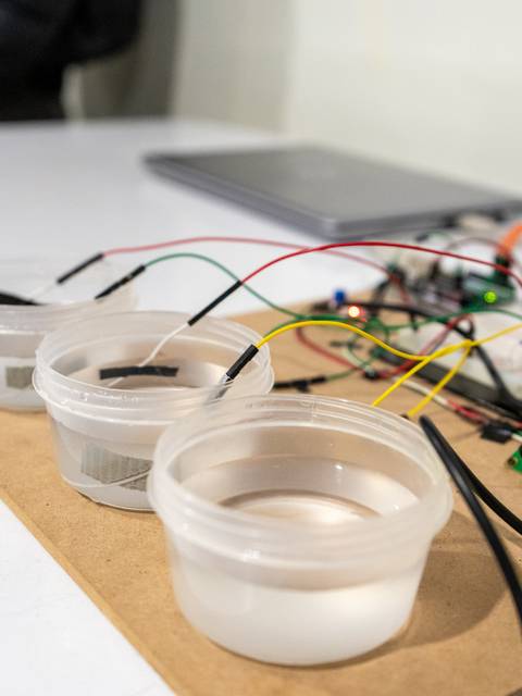 La imagen muestra tres recipientes transparentes conectados a cables y dispositivos electrónicos sobre una superficie blanca.