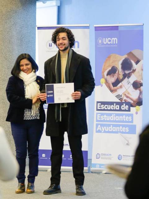 Un hombre y una mujer posan juntos mientras él sostiene un certificado en un evento académico.