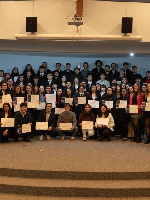 Un grupo de personas posando en un evento, sosteniendo diplomas en una sala de actos.