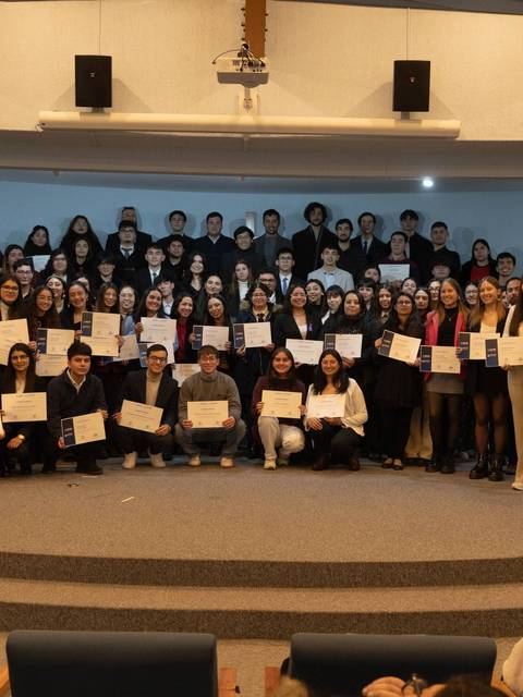 Un grupo grande de personas sostiene certificados en un evento de graduación.