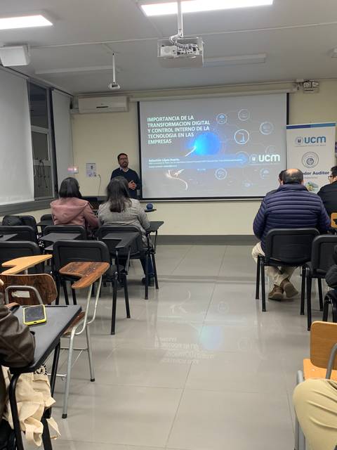 Un conferencista está presentando en un aula con varios asistentes sentado en las mesas.