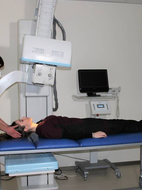 Un joven ajusta un equipo de rayos X mientras una persona está recostada en una camilla.