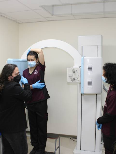 Un grupo de personas en un entorno médico, donde una persona está siendo atendida para un examen con un equipo de rayos X.