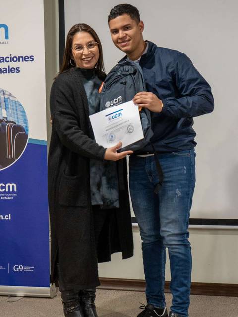 Una mujer y un hombre posan sonrientes mientras sostienen un certificado en un evento de entrega de reconocimientos.