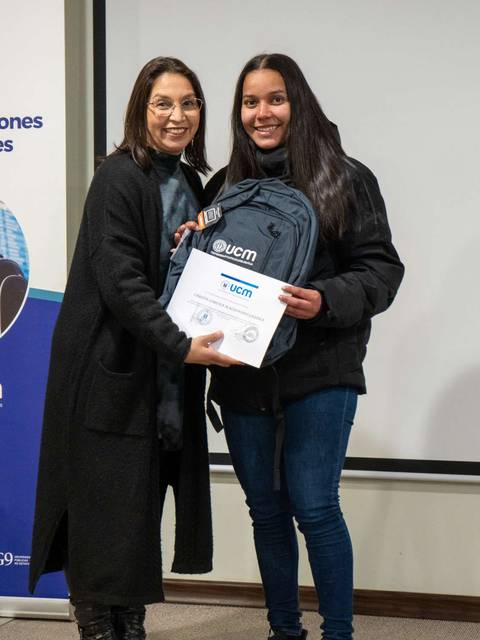 Una mujer y una joven sonríen mientras posan con un regalo en un evento.