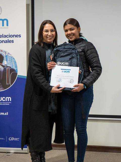 Dos mujeres sonríen mientras una sostiene un certificado en un evento.