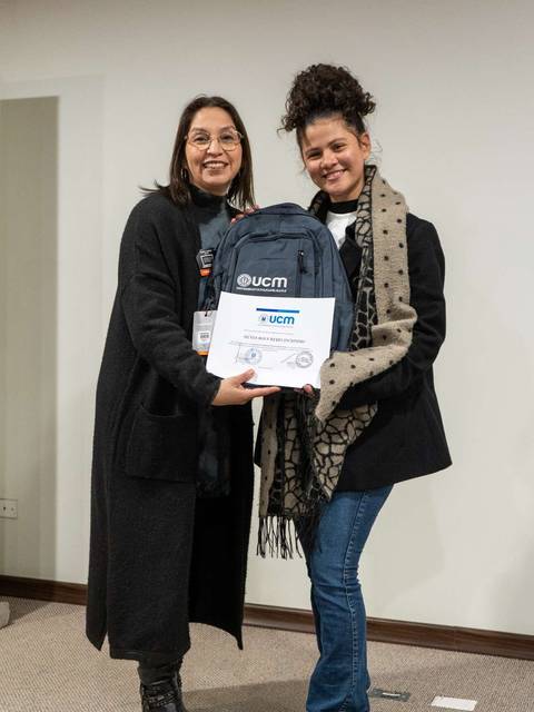 Dos mujeres posan juntas sosteniendo una mochila y un certificado.