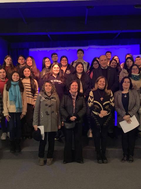 La imagen muestra a un grupo numeroso de personas posando juntas en un escenario con fondo iluminado en azul.
