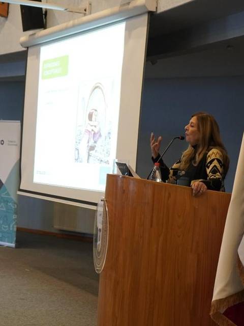 Una mujer está dando una presentación en un aula mientras se proyecta una diapositiva en una pantalla.