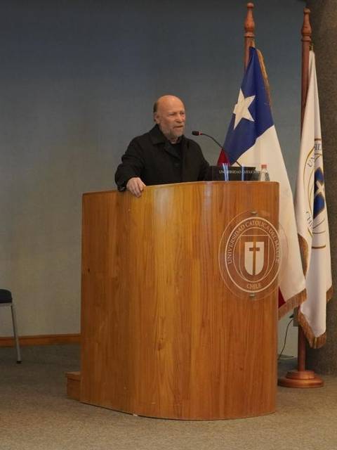 Un hombre está hablando en un podio en un evento oficial, rodeado de banderas.