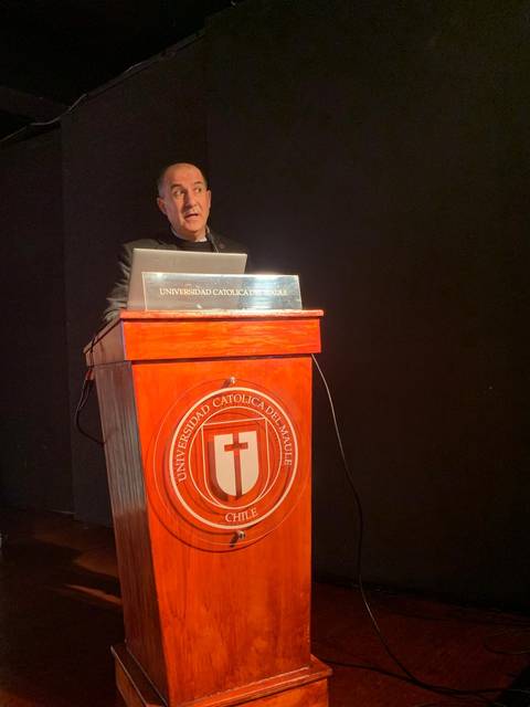 Un hombre está hablando desde un podio en un evento en la Universidad Católica de Chile.