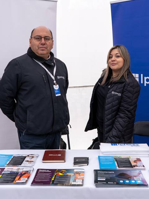 Dos personas posan en un stand con materiales promocionales.