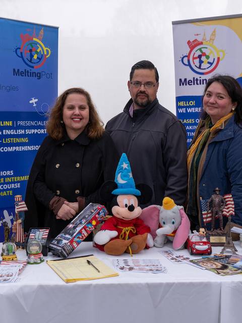 Tres personas están de pie junto a una mesa decorada con diversos objetos y banderas, representando una actividad cultural o educativa.
