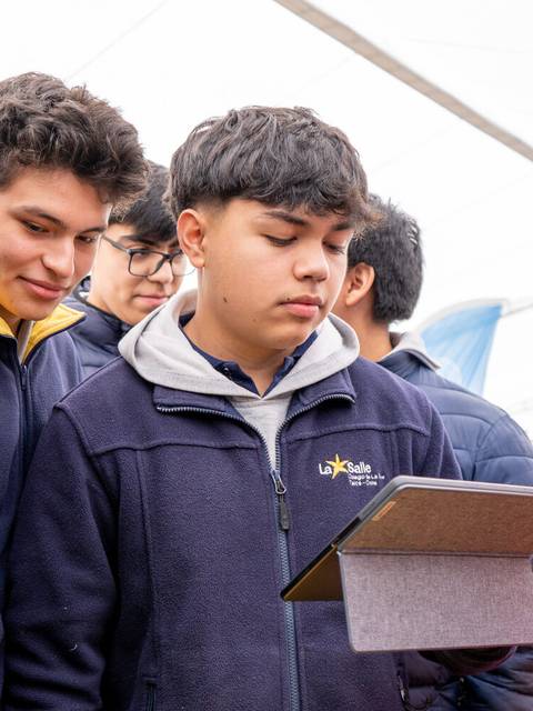 Un grupo de jóvenes se observa mientras uno de ellos revisa una tablet en un evento.
