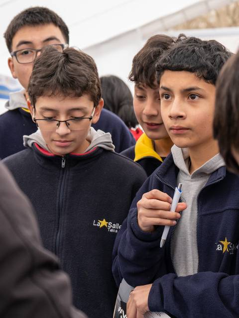 Un grupo de adolescentes escucha atentamente a un adulto en un evento educativo.