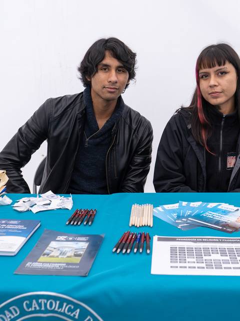 Dos personas se encuentran sentadas detrás de una mesa con materiales promocionales.