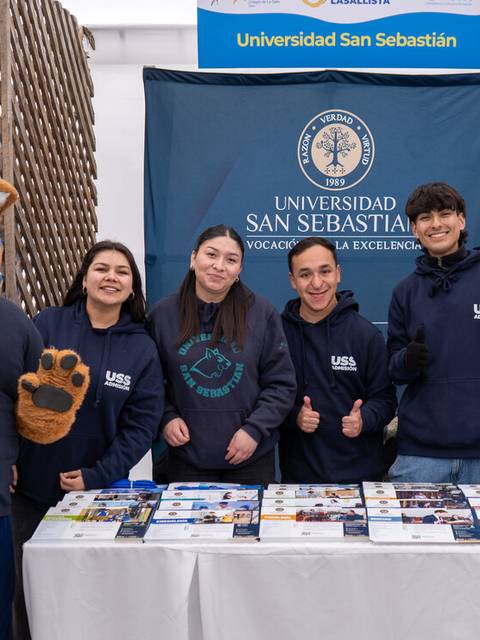 Un grupo de personas sonrientes en un stand de la Universidad San Sebastián en un evento.